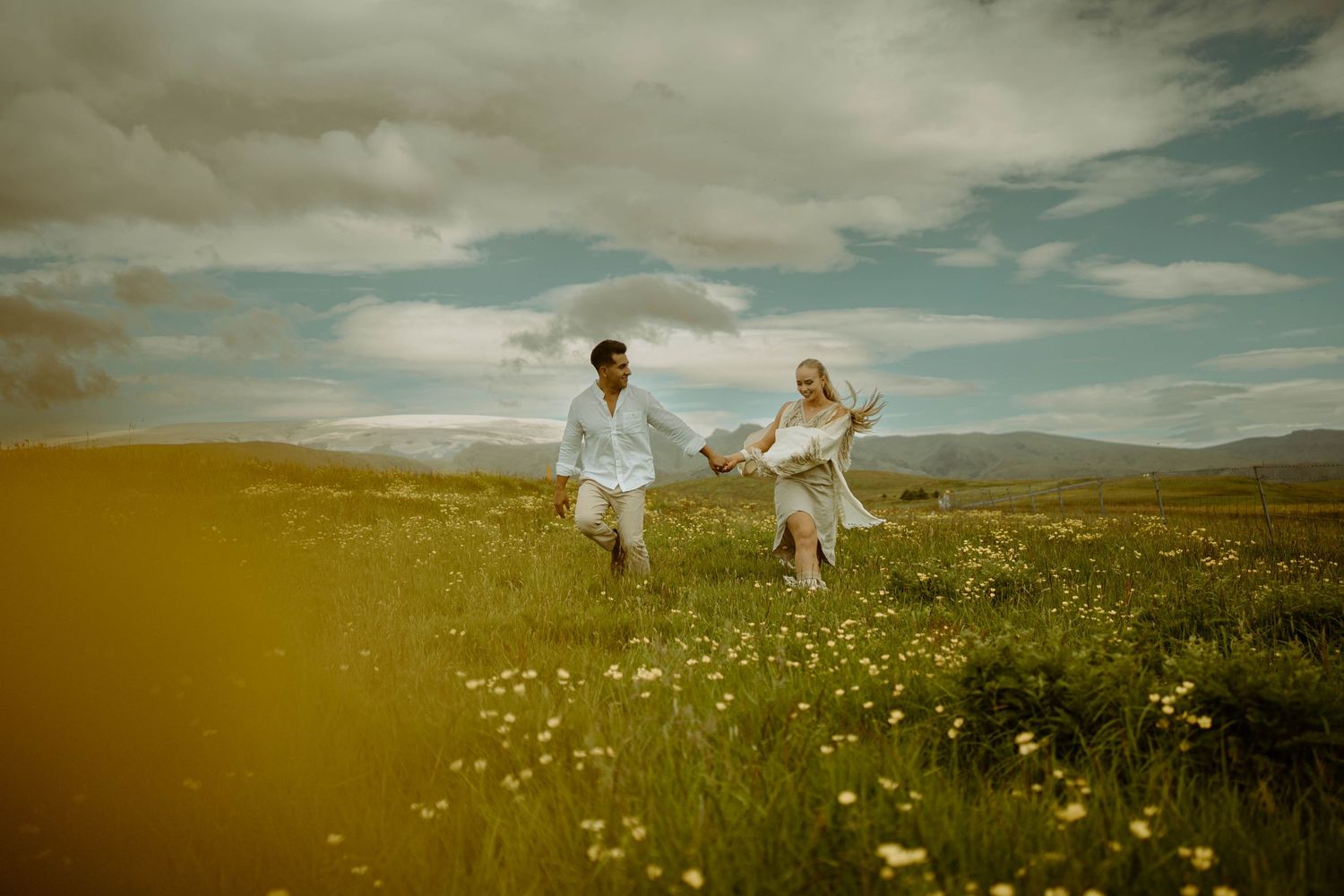 A couple runs through a sunlit meadow filled with wildflowers in Iceland.