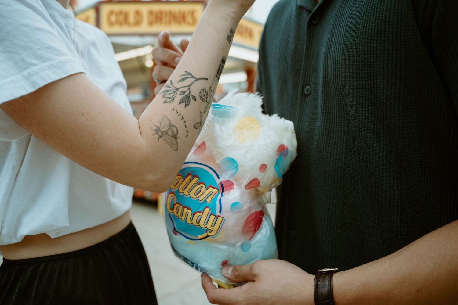 Tattooed arms holding cotton candy outdoors at K-Days in Edmonton, Alberta.