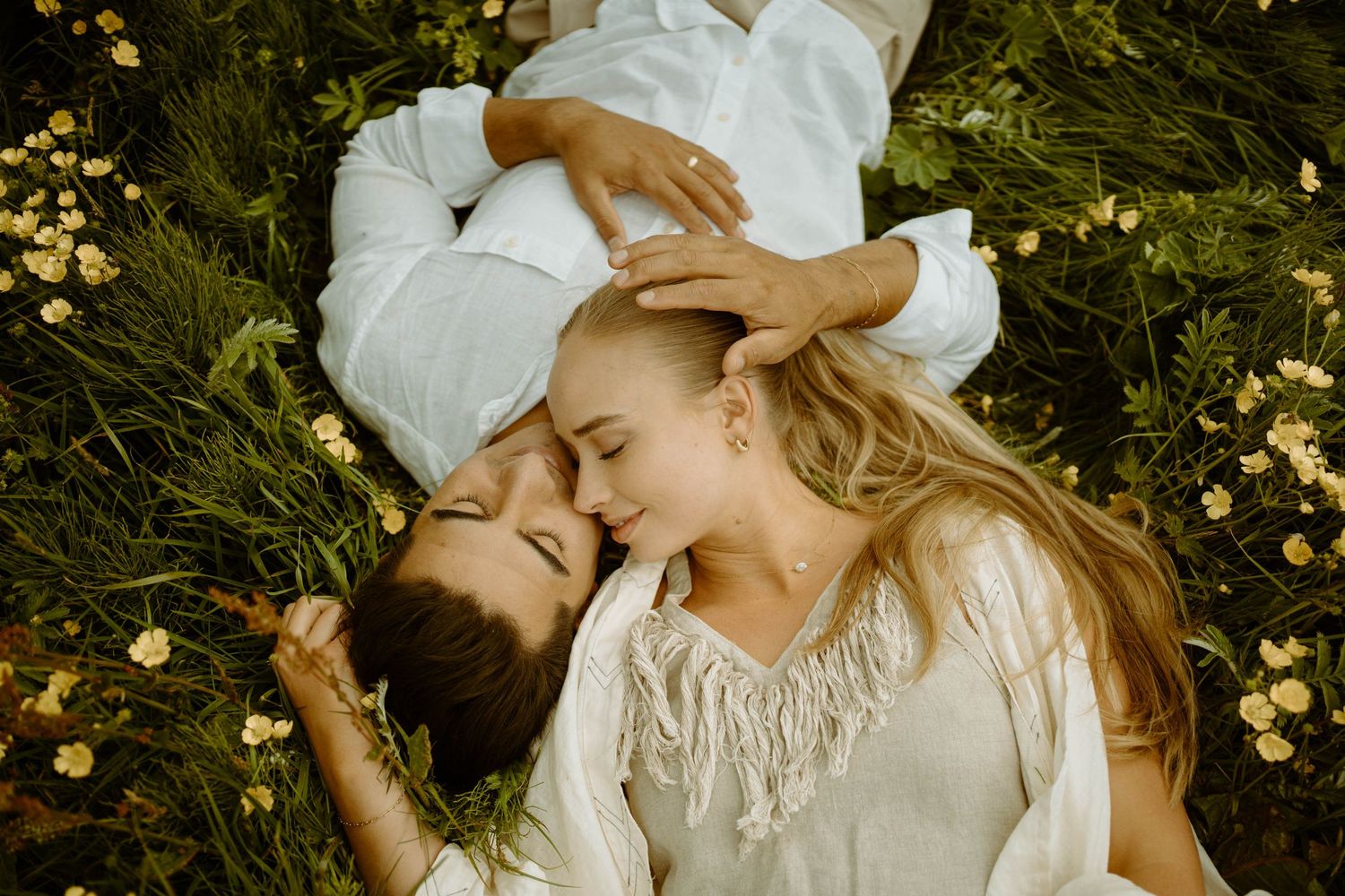 Couple in white clothing lying among yellow flowers in intimate embrace in Iceland.