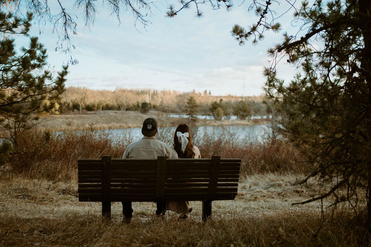 A couple sits together on a wooden bench overlooking a peaceful lake view.