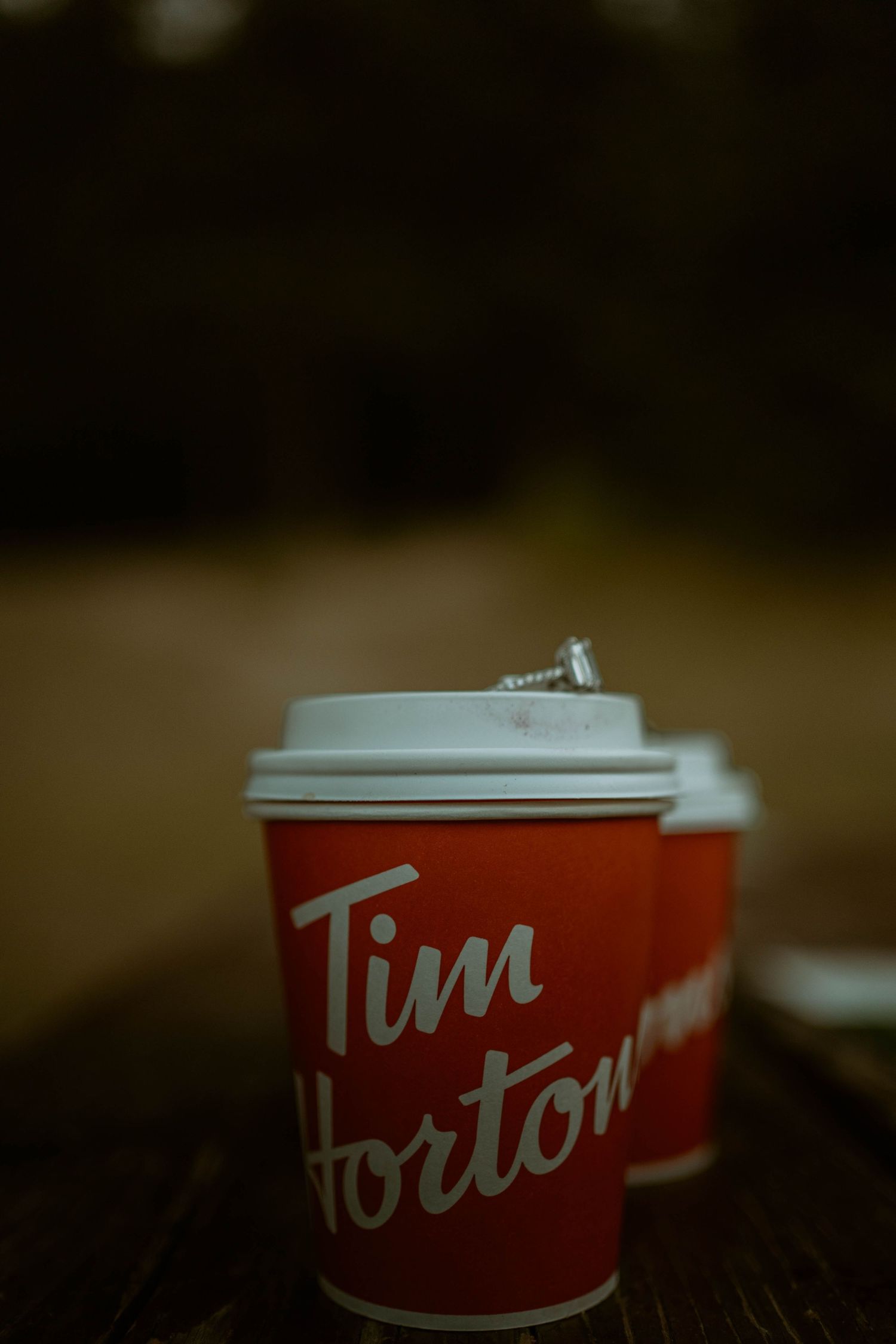 Tim Hortons coffee cup with engagement ring balanced on lid in moody lighting.