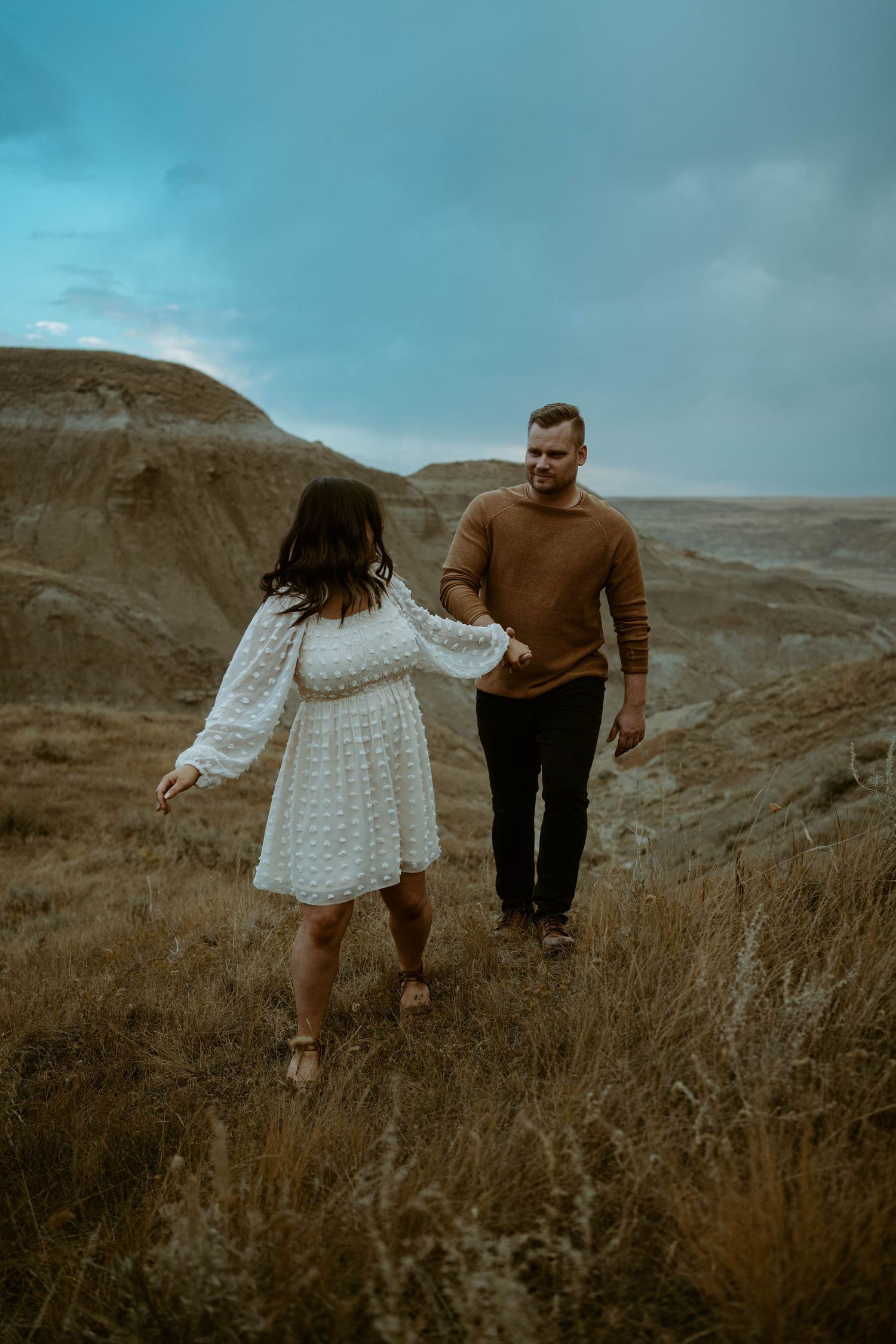 Couple holding hands while walking through scenic mountain landscape.
