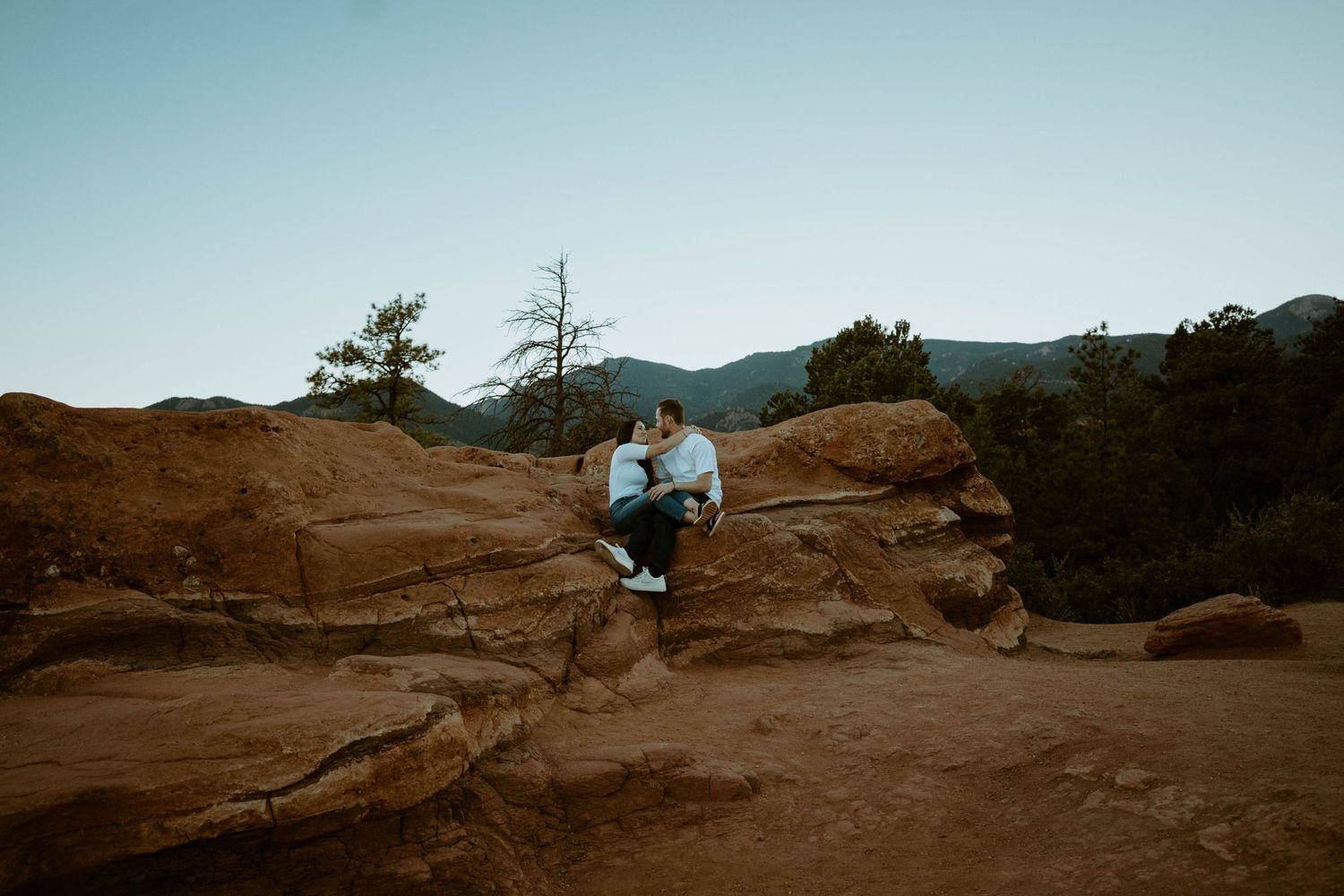 A couple sits together on red rock formations against a mountain backdrop in Colorado.