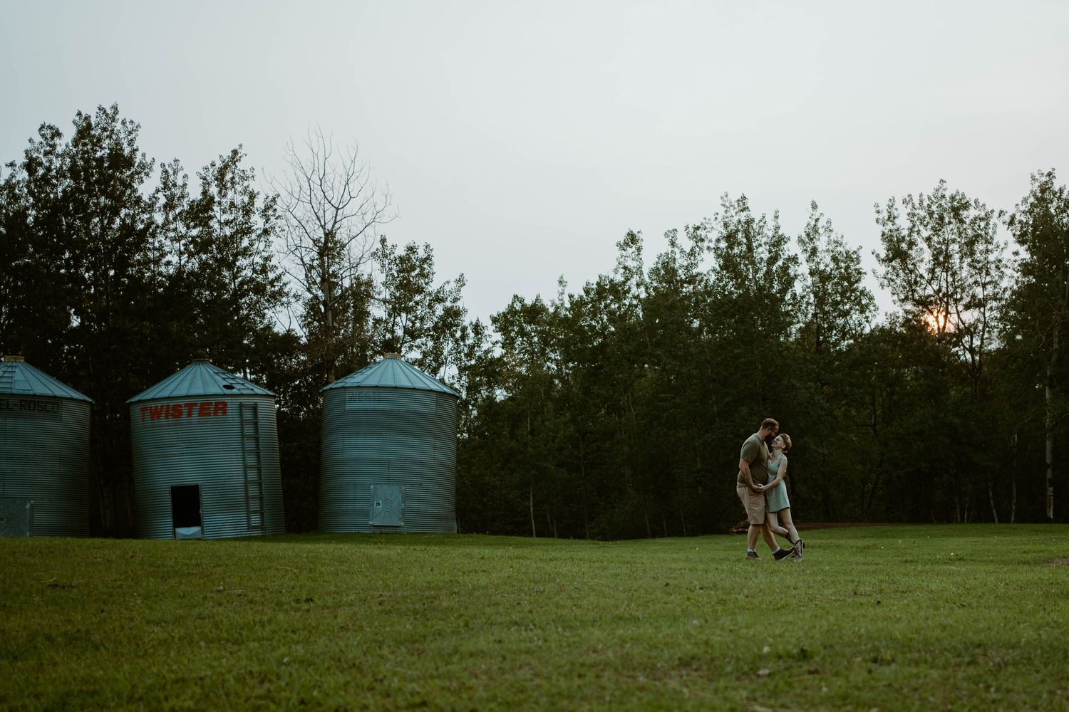 A romantic moment unfolds near blue storage silos at dusk in Southern Alberta.