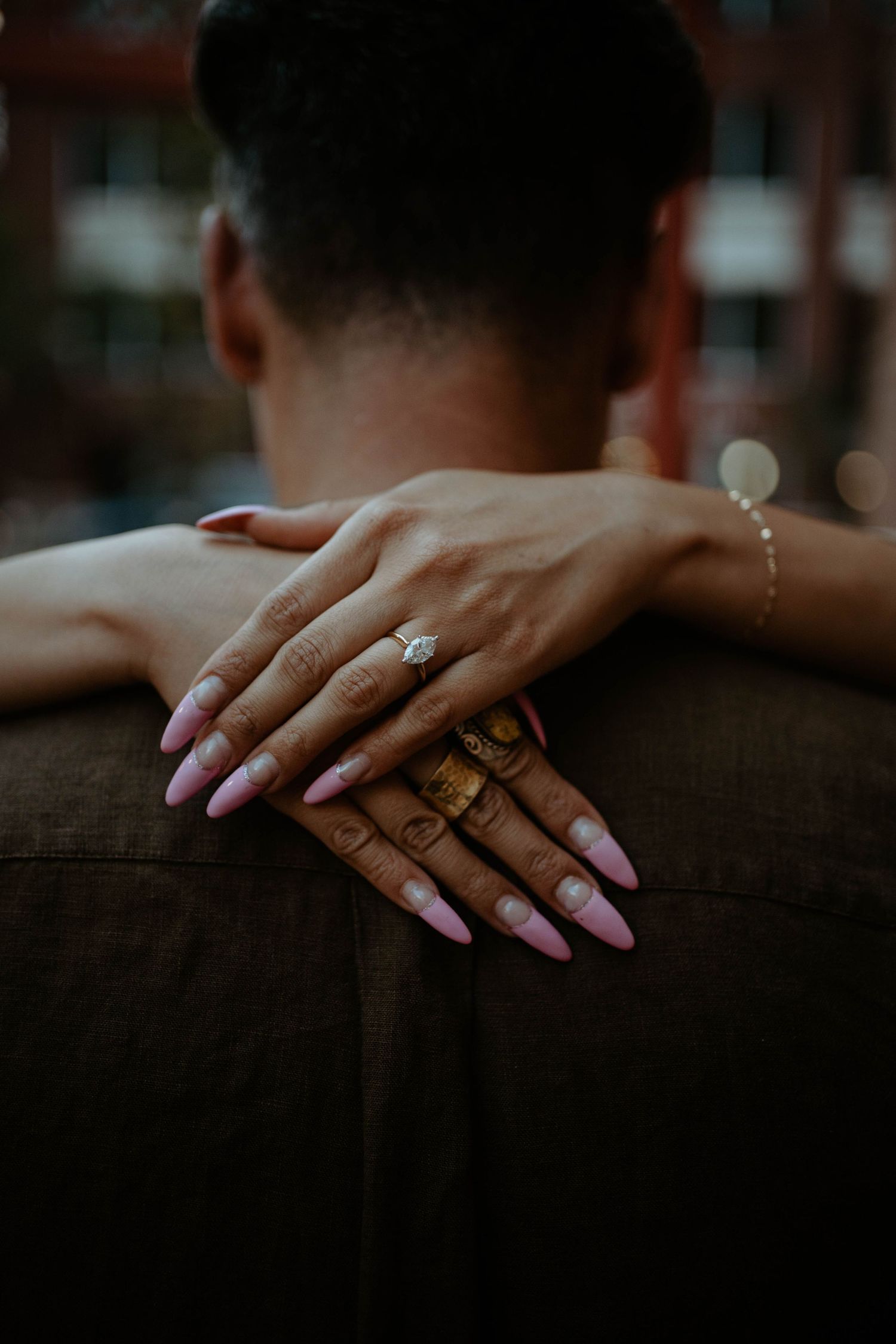Close-up shot of hands with engagement ring and pink manicure resting on shoulder.
