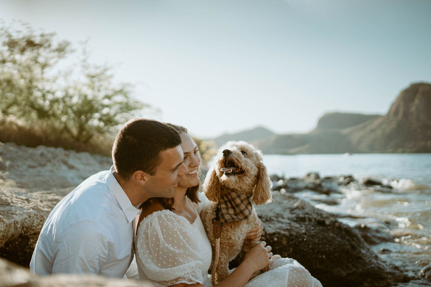 Casual beachside portrait with a happy dog joining the couple in white outfits.