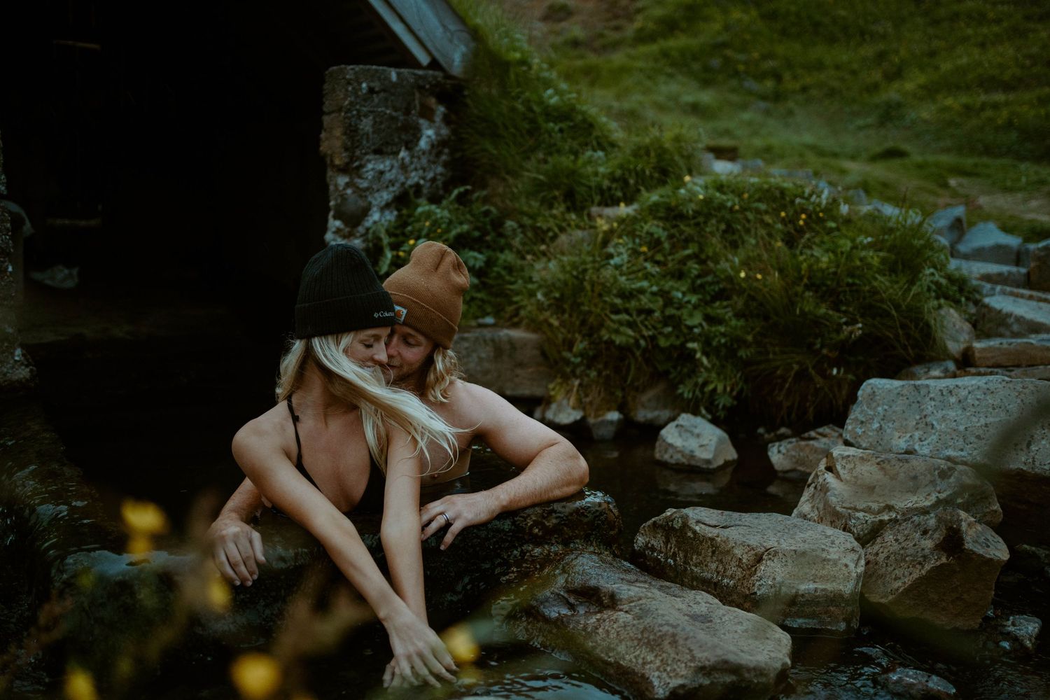 A couple relaxes by natural hot springs in a moody outdoor setting in Iceland.