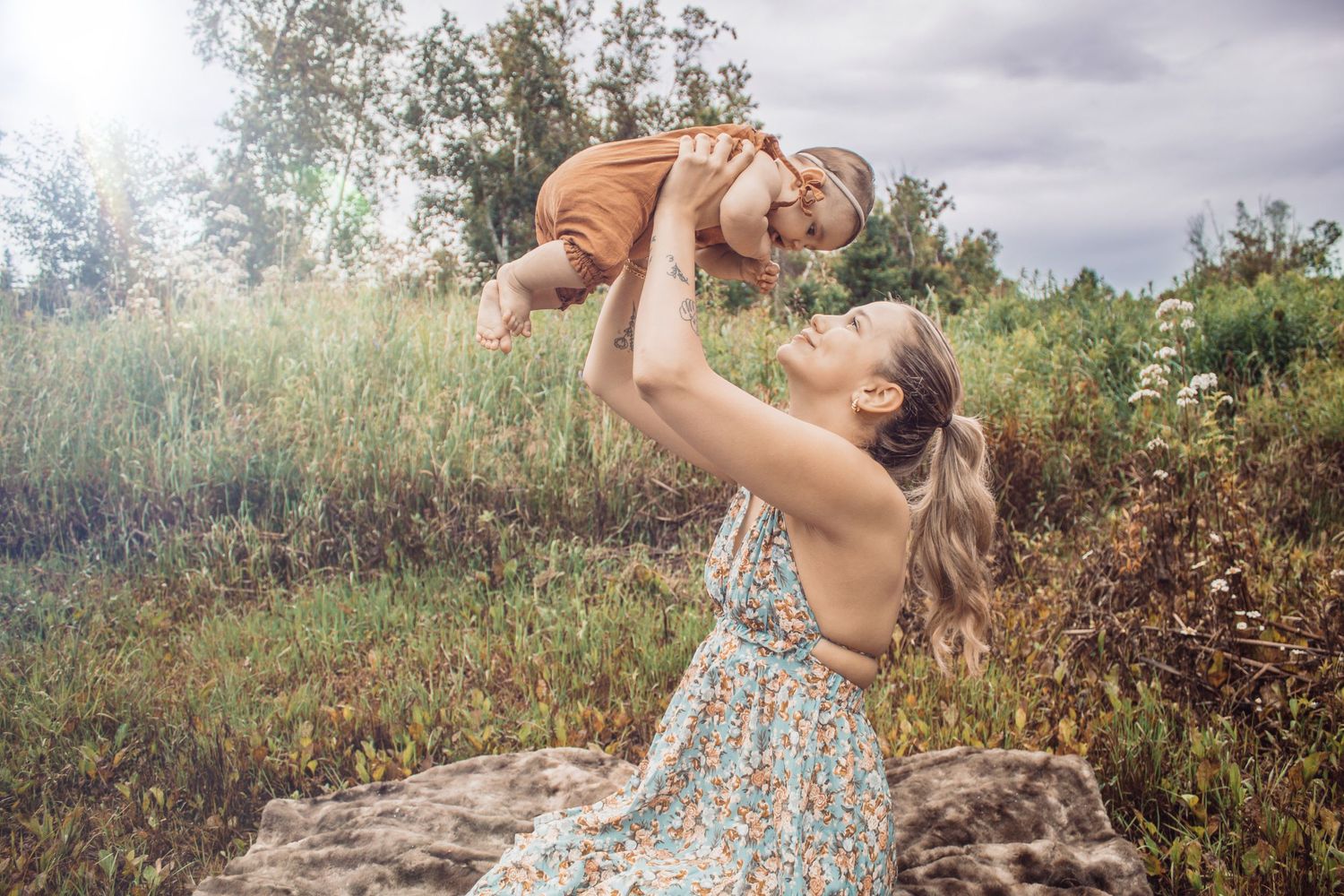 young mom and baby girl, mom lifting baby in air, looking up at her smiling, outdoor photoshoot.