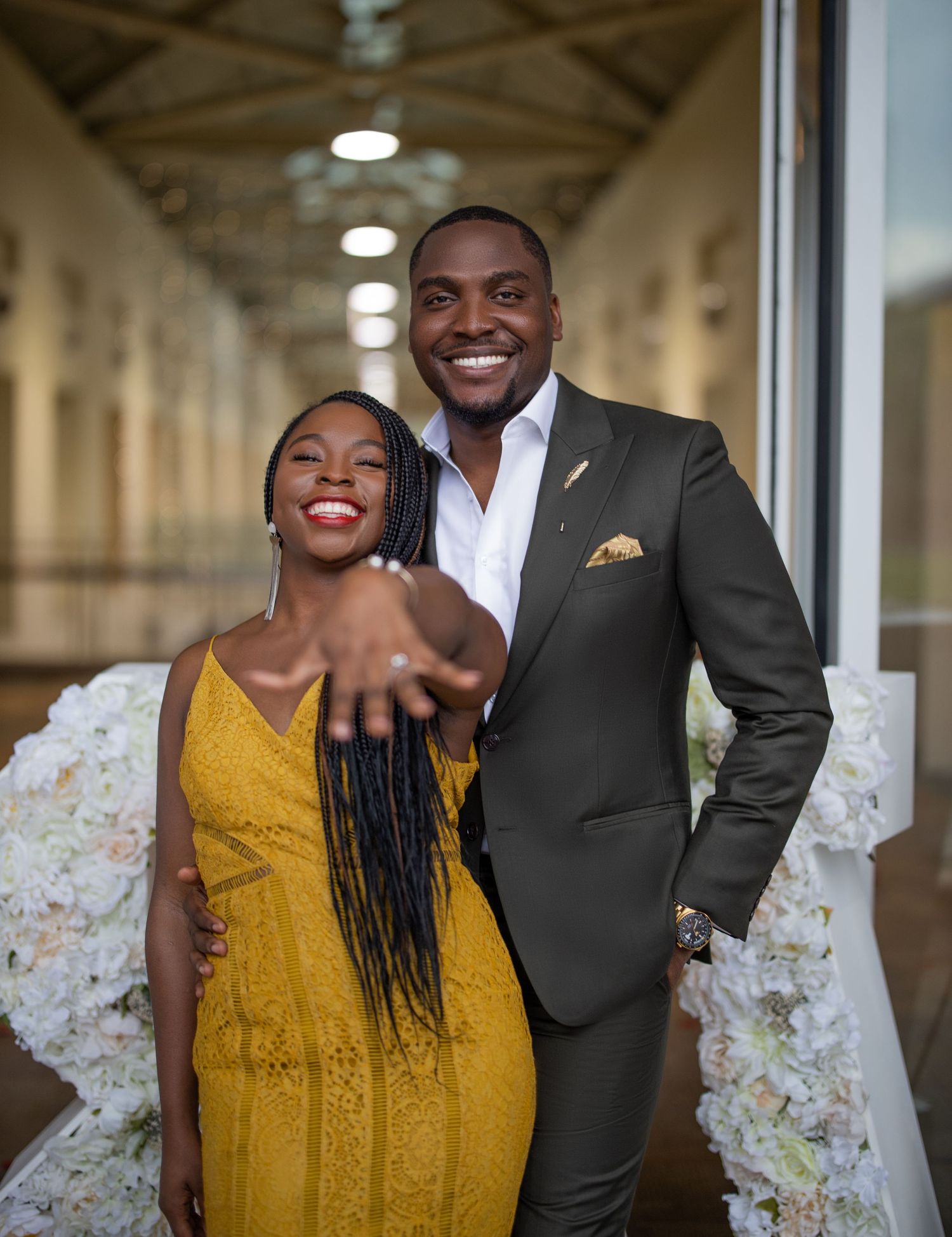 A couple shares a joyful moment in a bright hallway at a formal event.