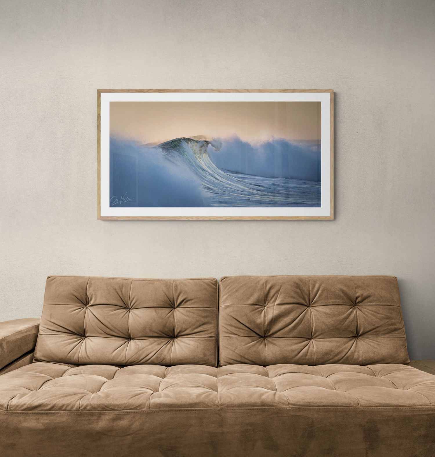 A dramatic surfing photograph displayed above a tufted brown sofa in a contemporary room setting.