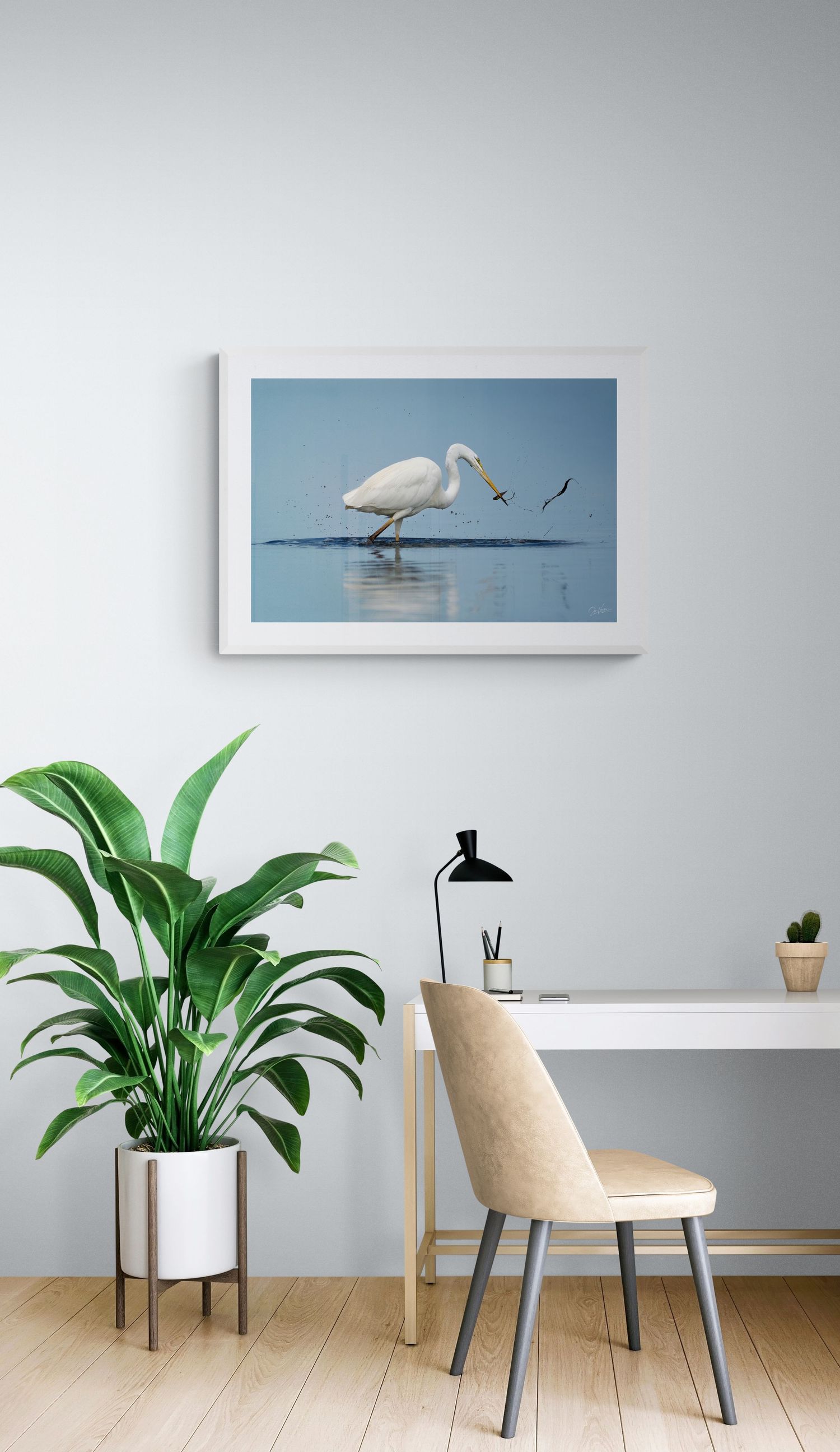 White egret wading in shallow water, framed print above minimalist desk with house plant.