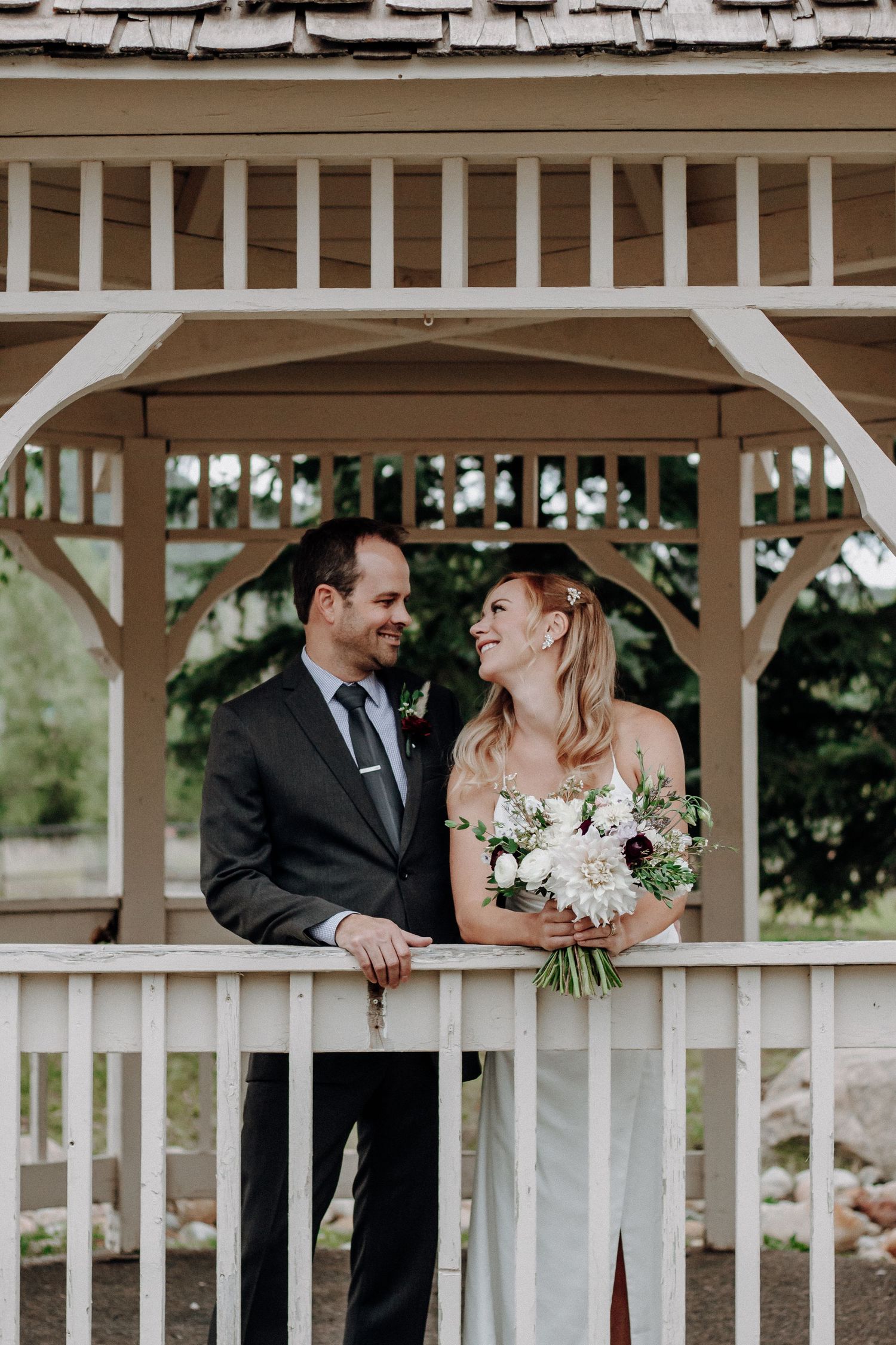 A romantic moment captured under a wooden gazebo with wedding attire and floral bouquet.