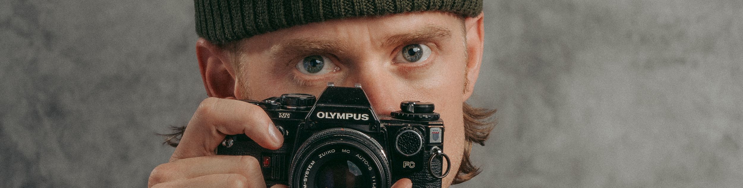 Close-up shot of a photographer wearing a beanie and holding a vintage camera.