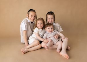Four siblings in coordinating white and beige outfits posed together on neutral background.