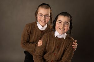 Studio portrait in matching brown sweaters and white collars against dark background.