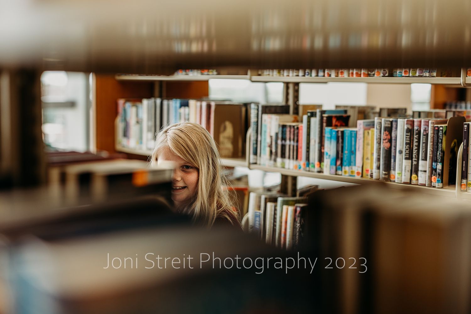 Library shelves filled with books captured through a blurred foreground frame.