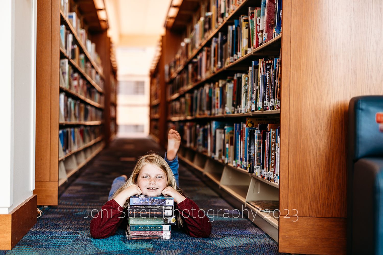Books line both sides of a long library aisle with carpeted floor.