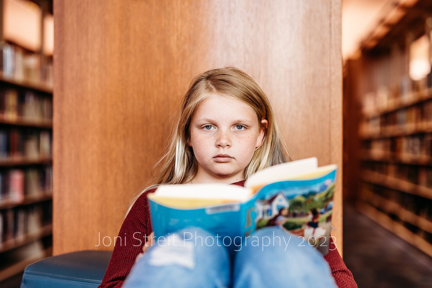 Library patron reads book while seated among wooden bookshelves.