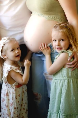 Young children touching and interacting with a pregnant belly in a sweet indoor portrait.