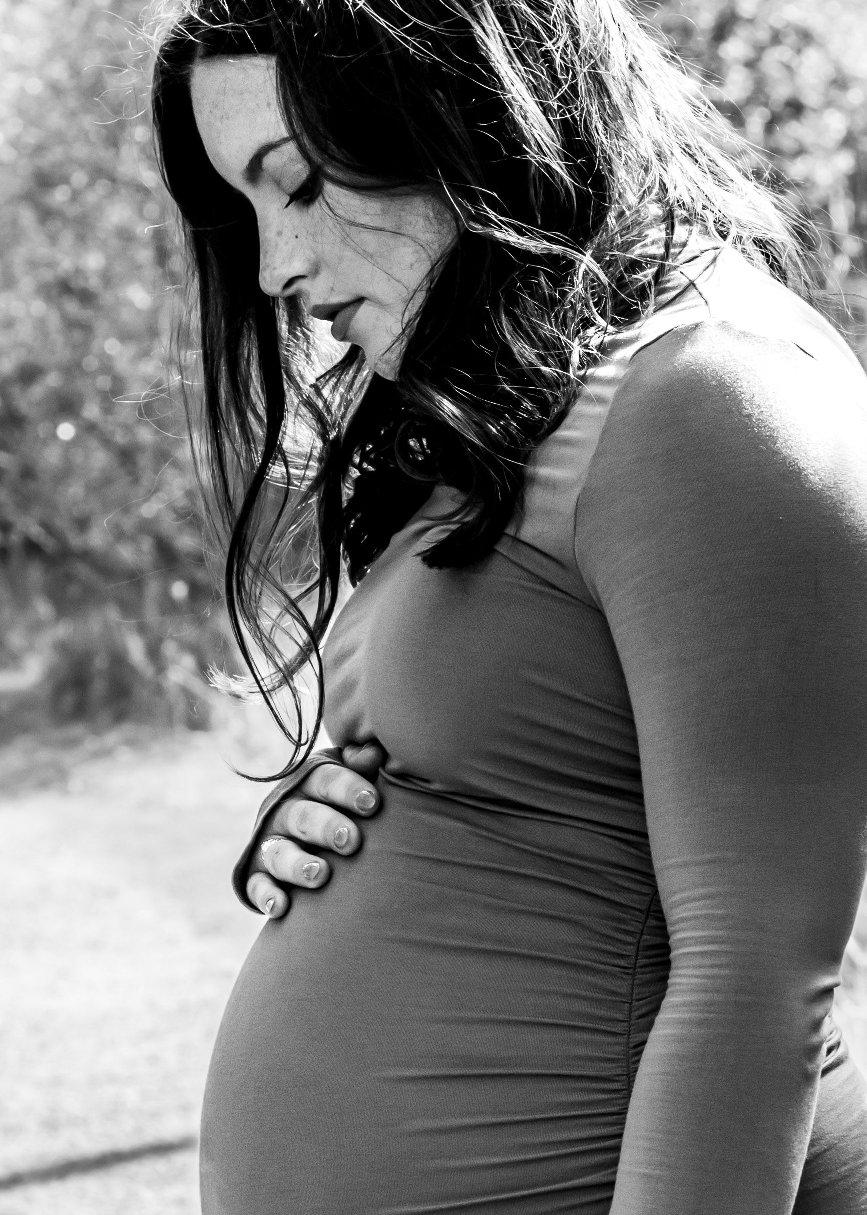 Black and white profile portrait of an expectant mother in a fitted top showing her baby bump.