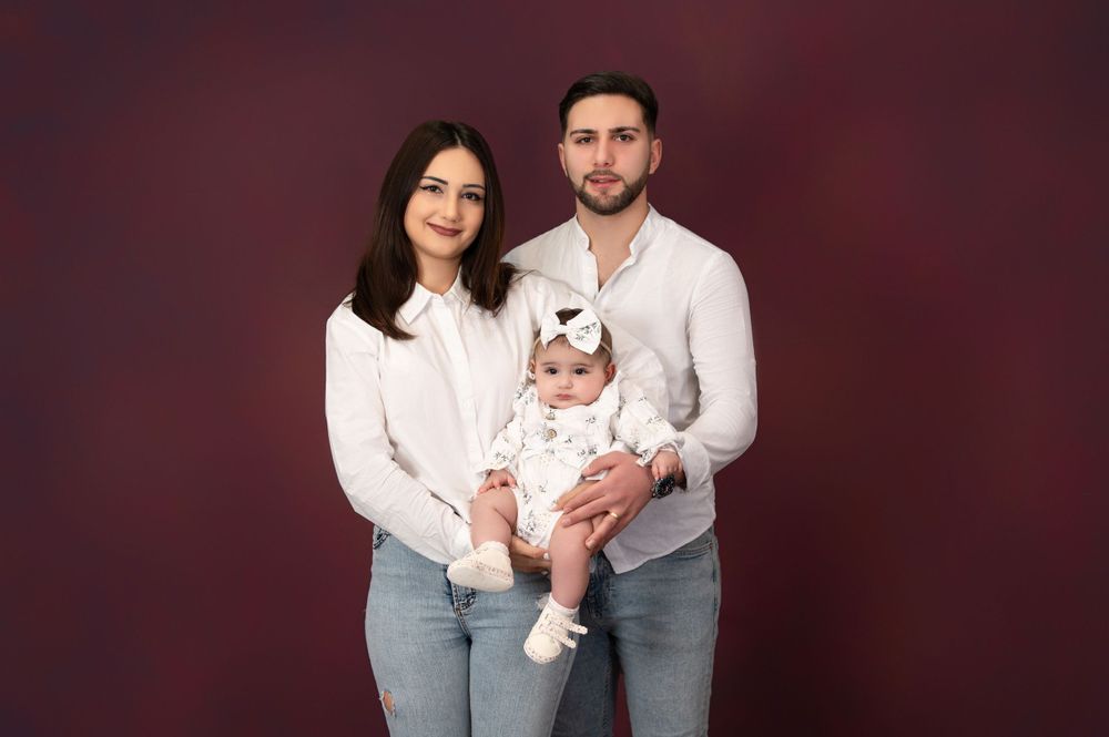 Family portrait session in coordinated white outfits against dark burgundy backdrop.