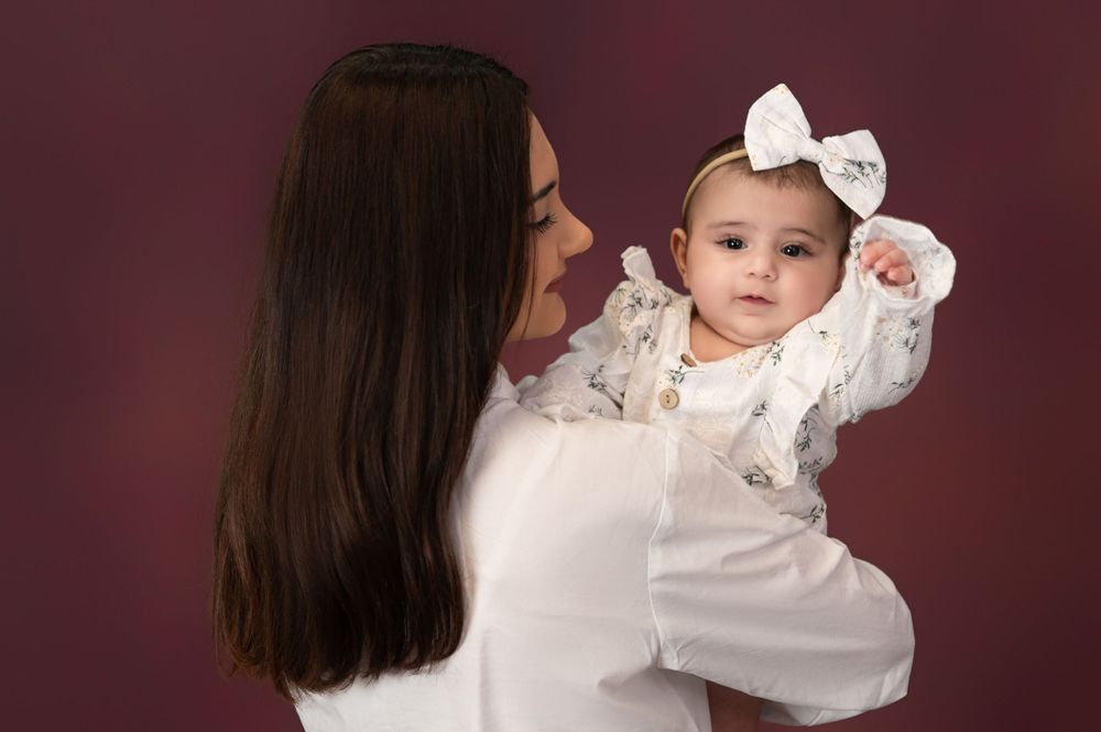 Baby in white dress with bow poses during professional portrait session.