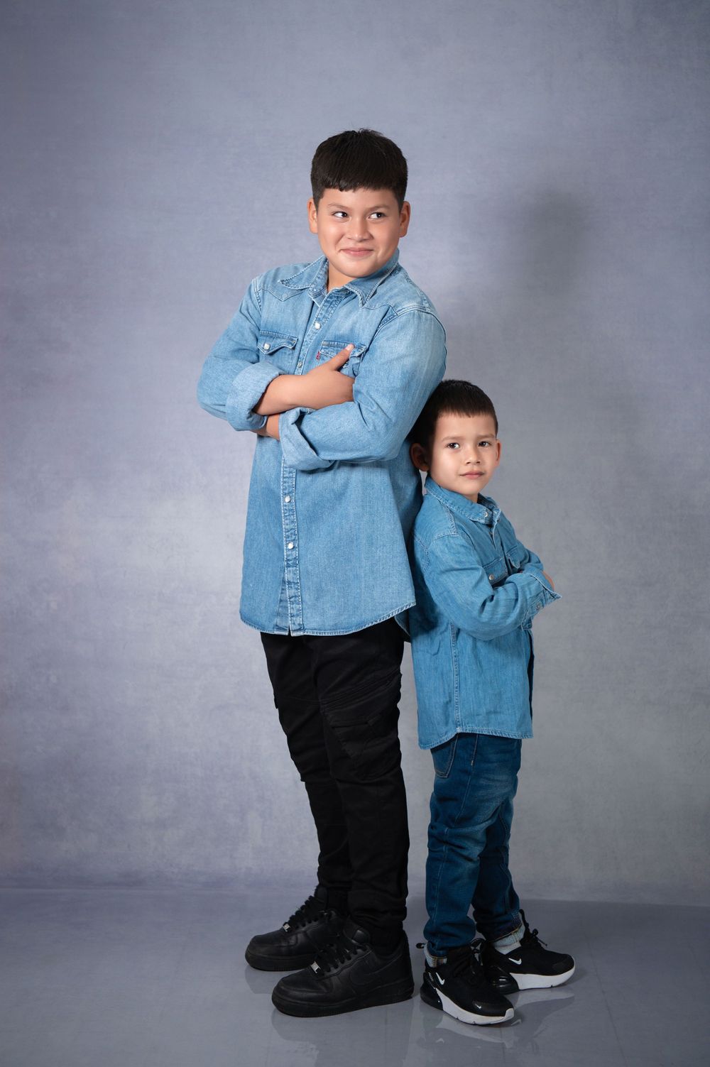 Two children posing in denim outfits against grey studio backdrop.