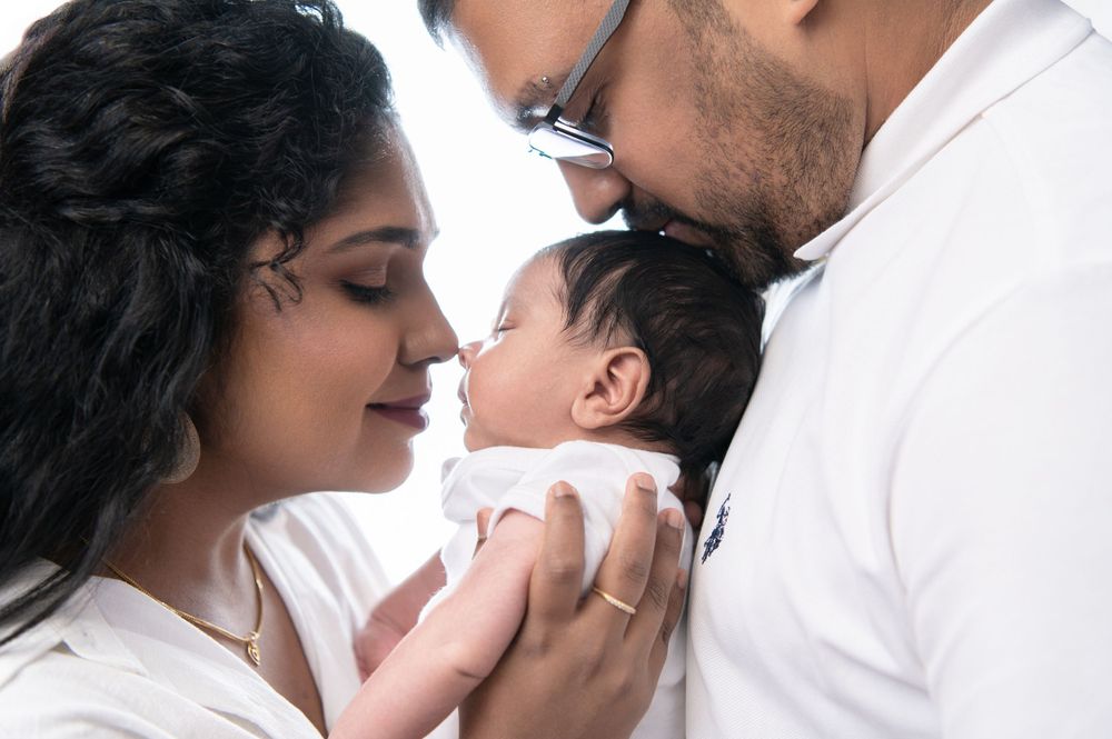 A tender moment with a newborn baby being cradled by parents against a white background.