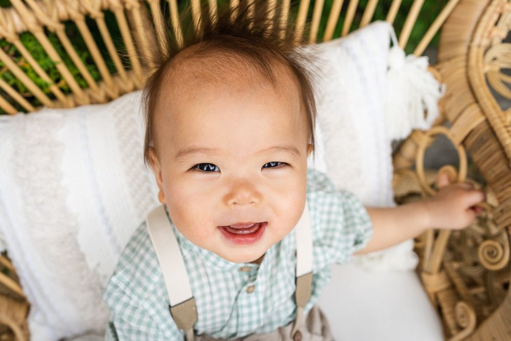 Birthday party photographer capturing smiling one year old sitting on a wicker chair in Seattle