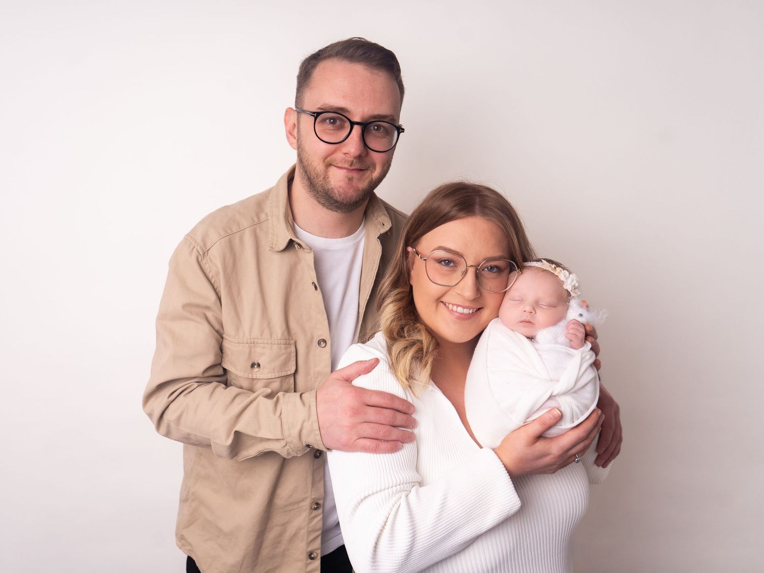 mum and dad with baby family photo with baby girl sleeping wrapped in white by doncaster heather katie photography.