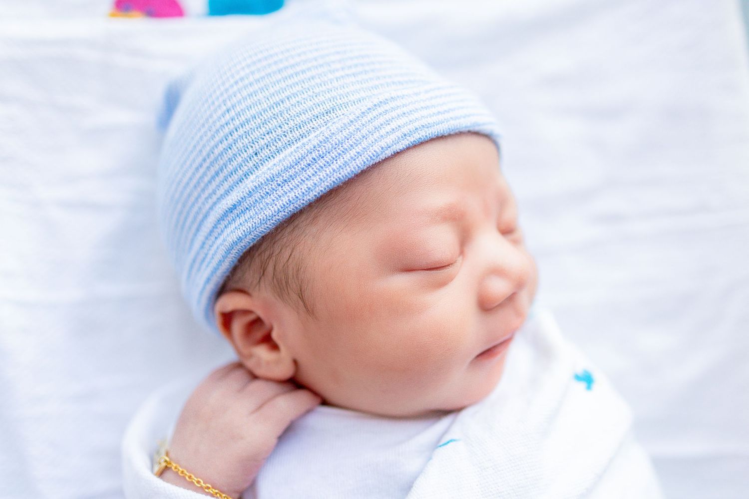 Peaceful newborn baby sleeping in blue knit hat on white blanket.