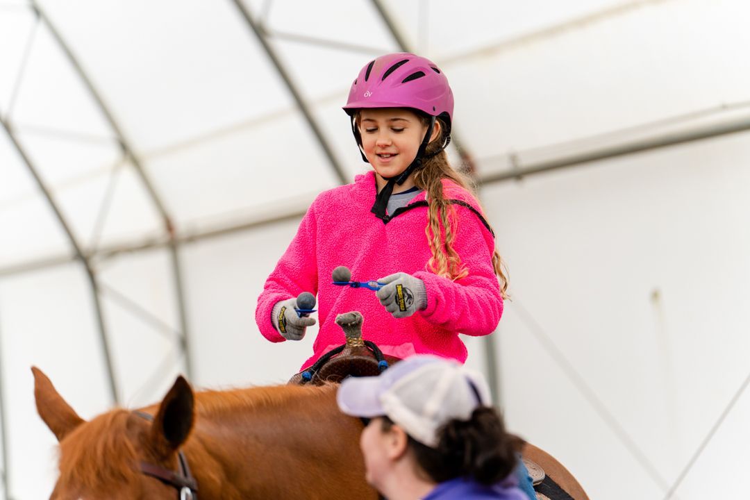 girl balances eggs on spoons while riding a horse