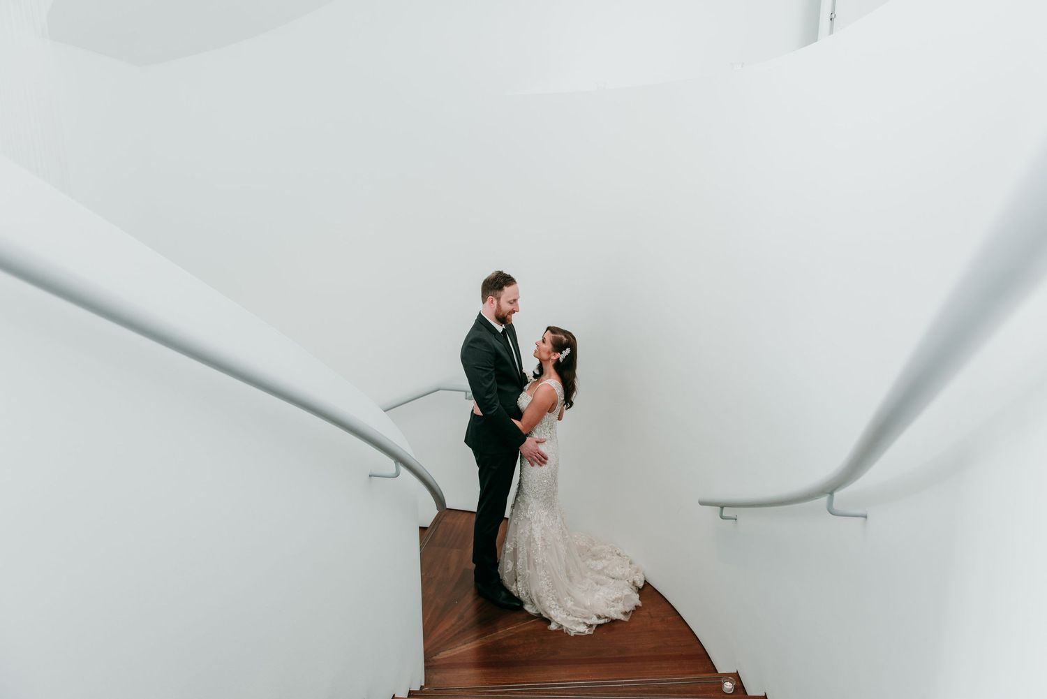 A bride and groom embrace on a staircase with curved white walls surrounding them at Maritime Parc.