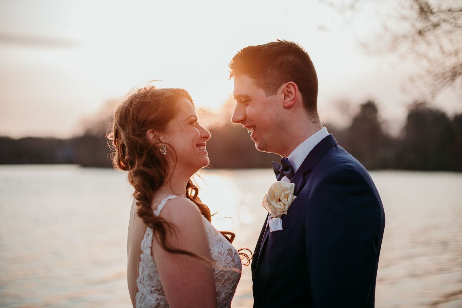 A romantic wedding couple shares an intimate moment at sunset by a serene lake at Indian Trail Club in New Jersey.