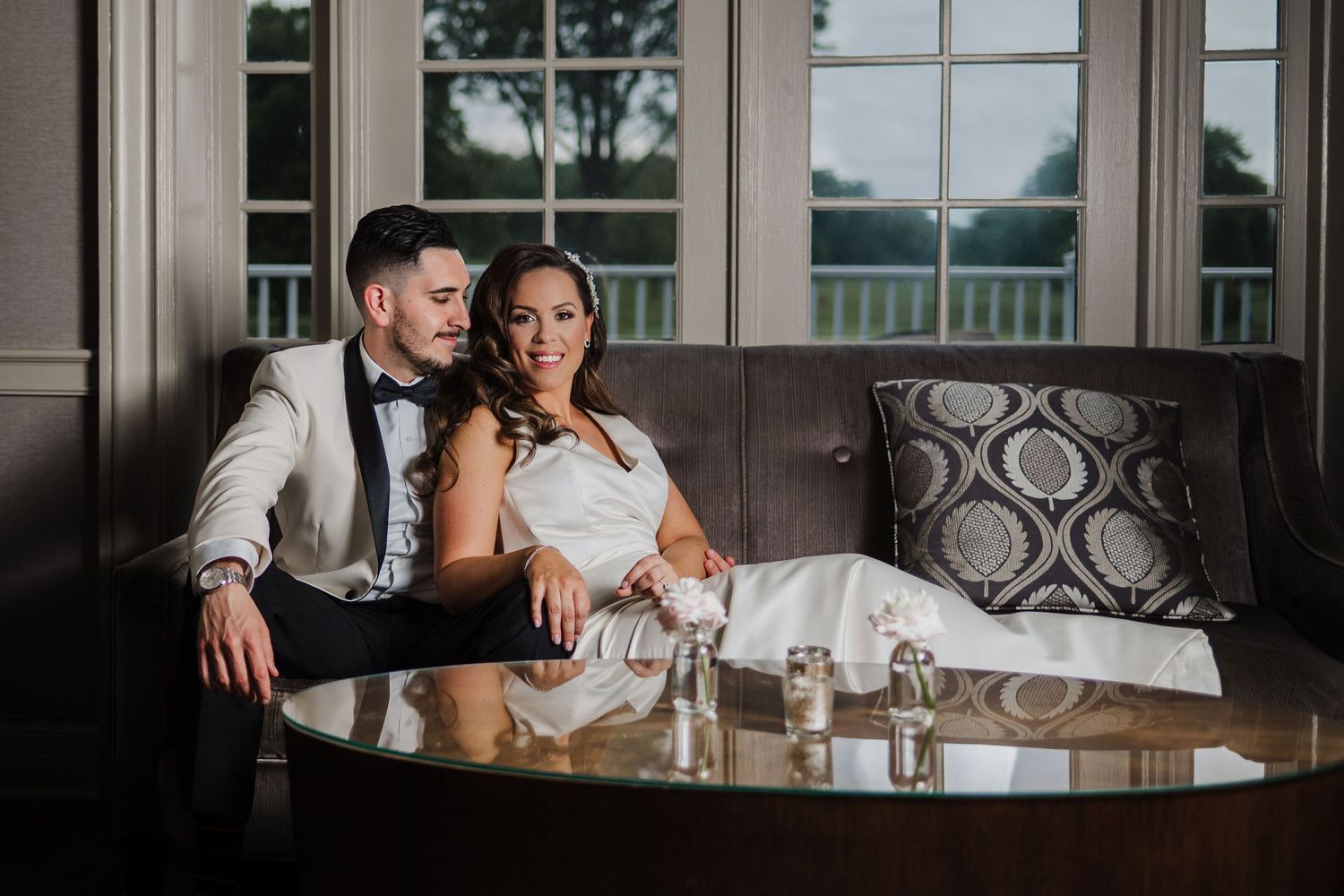 Elegant bride and groom relax together on brown leather couch during wedding reception near decorative table in Maplewood.