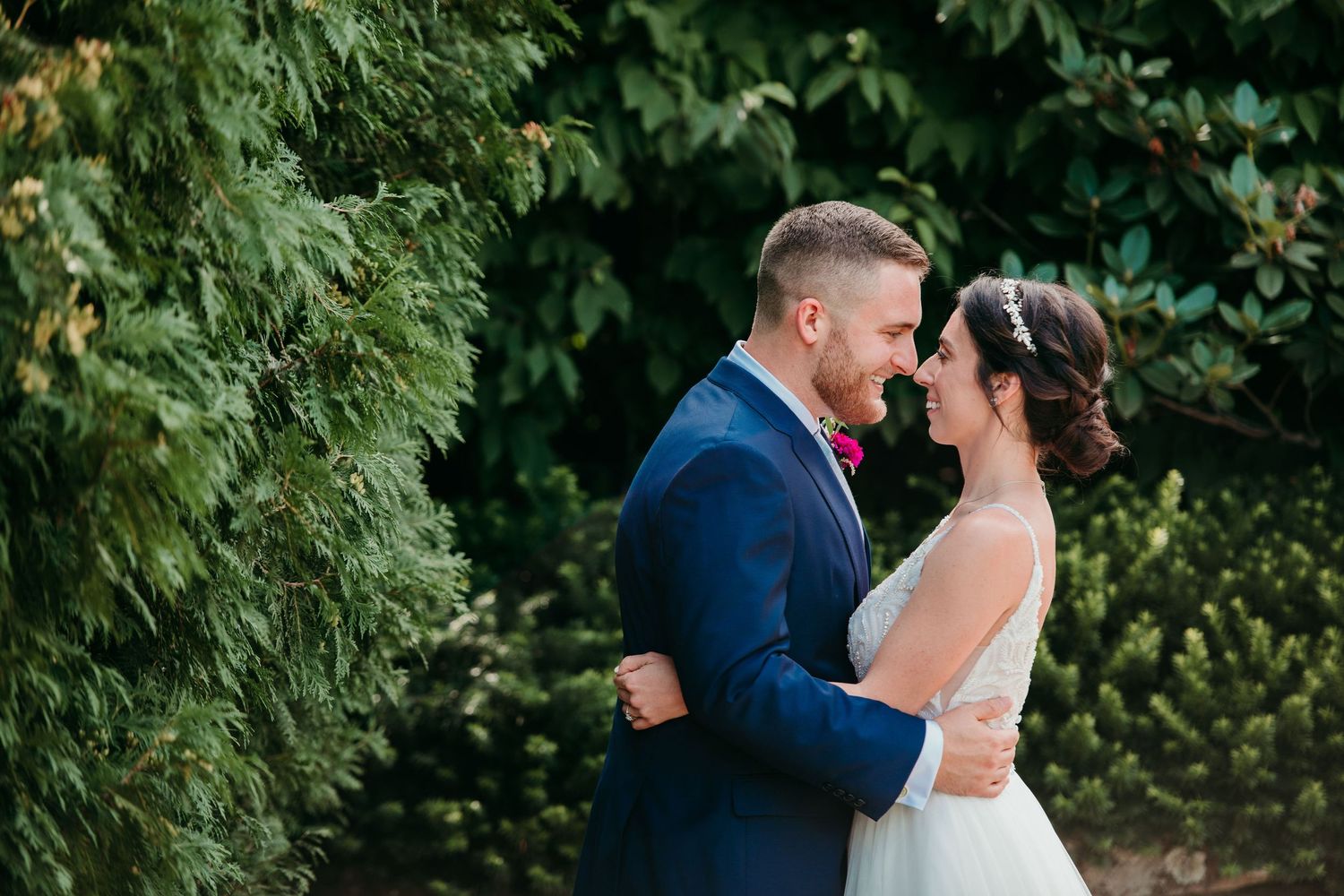 A happy couple shares an intimate moment during their wedding photoshoot amidst lush green foliage.