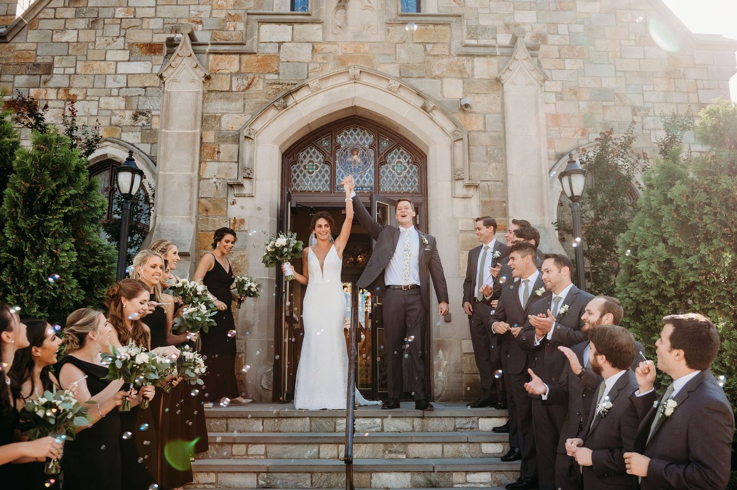 Wedding party celebrates on stone church steps as guests throw confetti during joyful exit celebration.