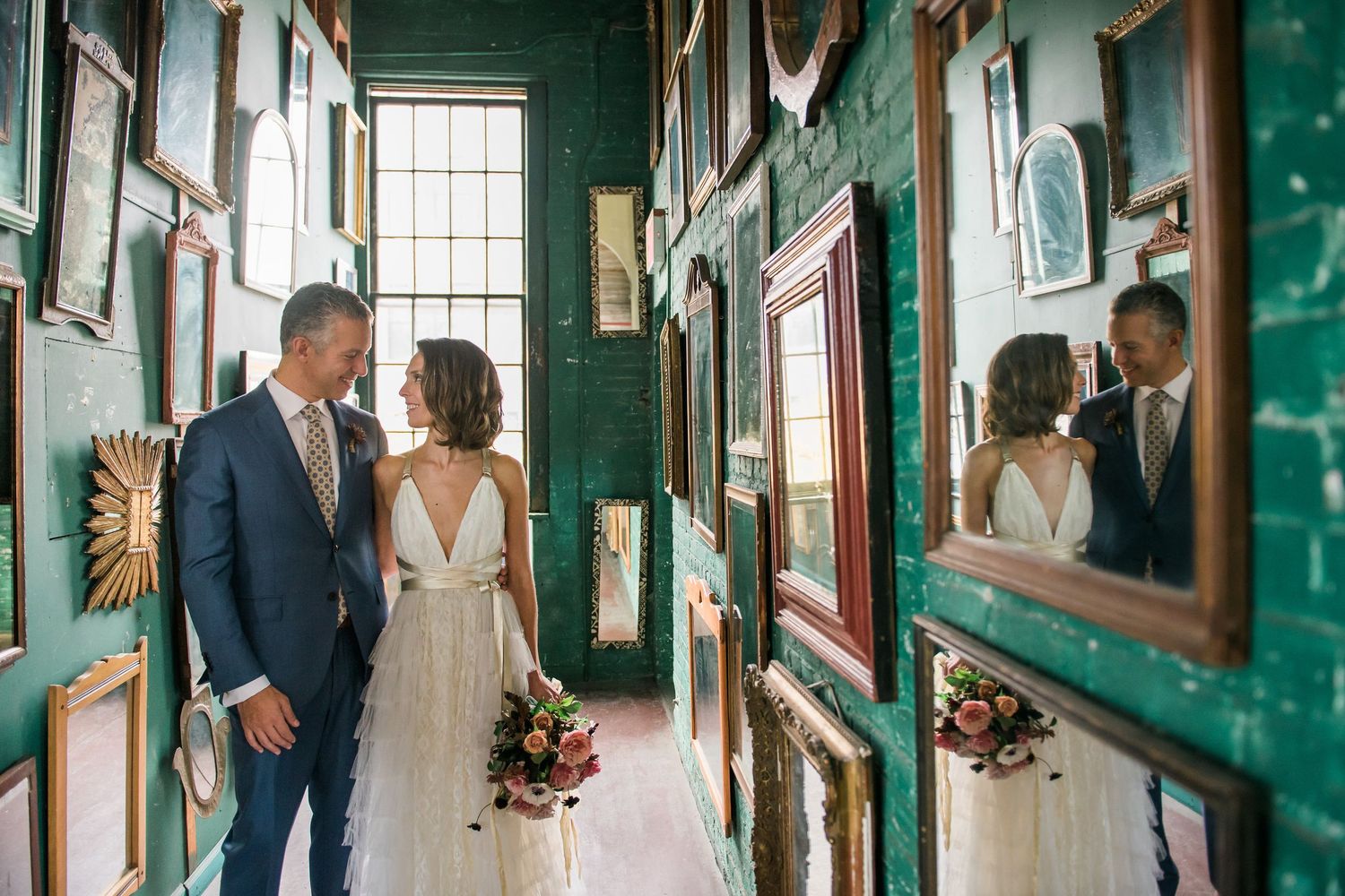 A couple on their wedding day poses in a vintage green hallway filled with antique mirrors and natural light in Long Island City.