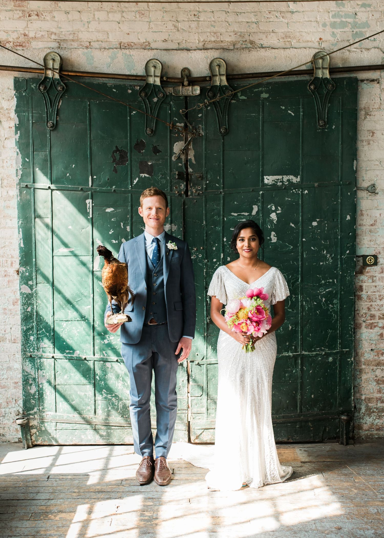 A couple stands together against a weathered green industrial door while sunlight streams across the floor in New York City.