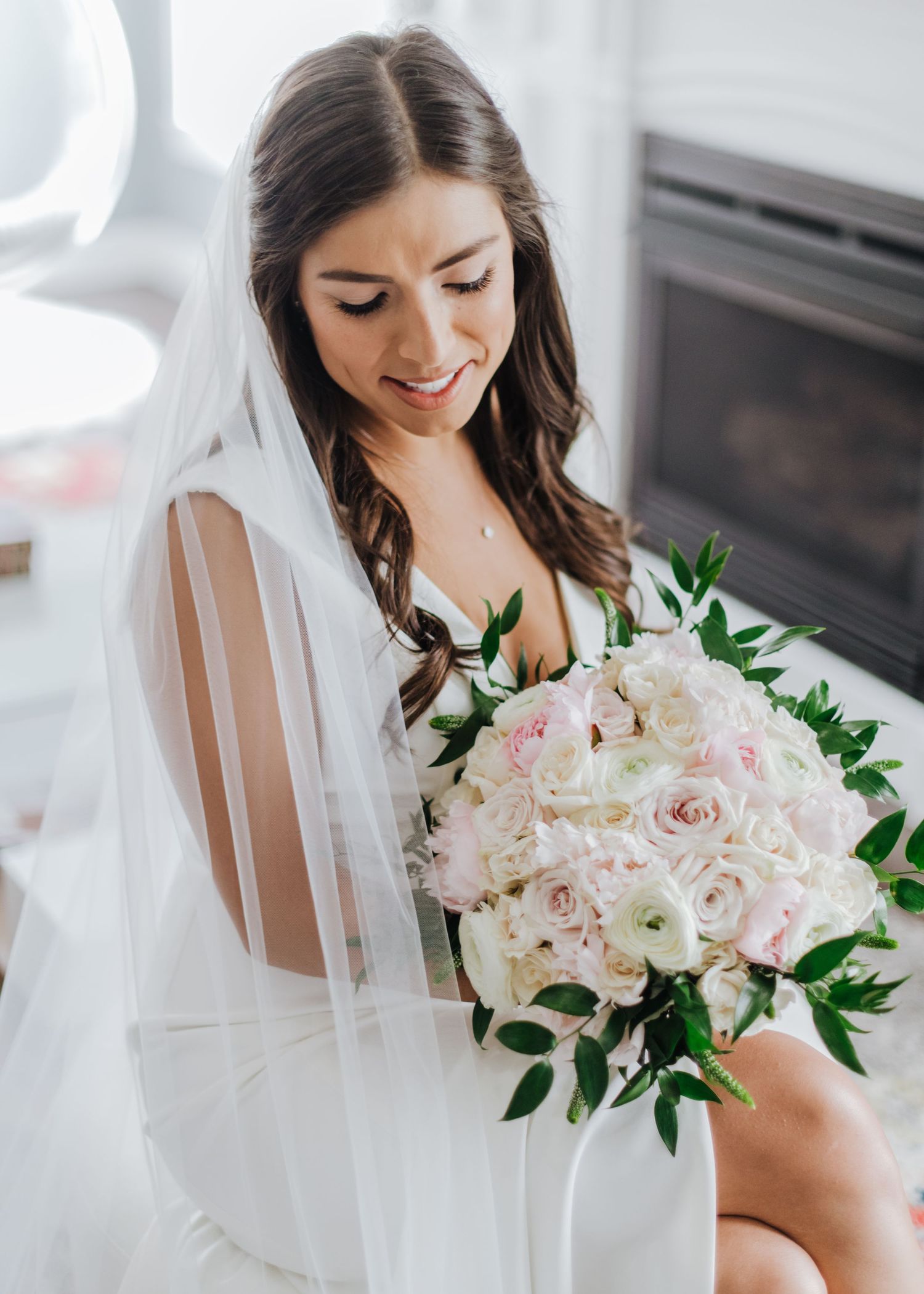 Bride in white dress and veil holds elegant pink and white rose bouquet with green foliage accents at the Ryland Inn.