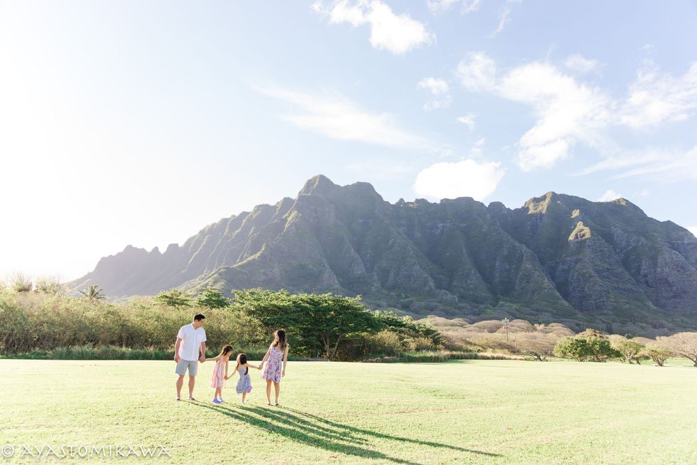 Family strolls across a grassy field with majestic Ko'olau mountains in the background.