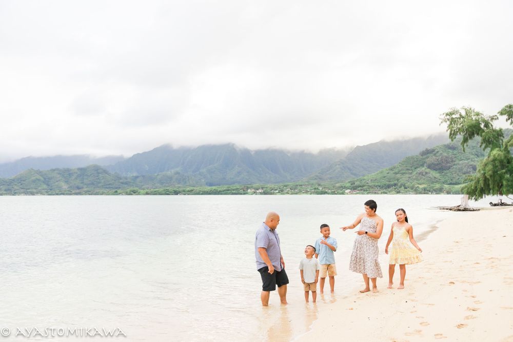 A group walks along a scenic Hawaiian beach with misty mountains in the background.