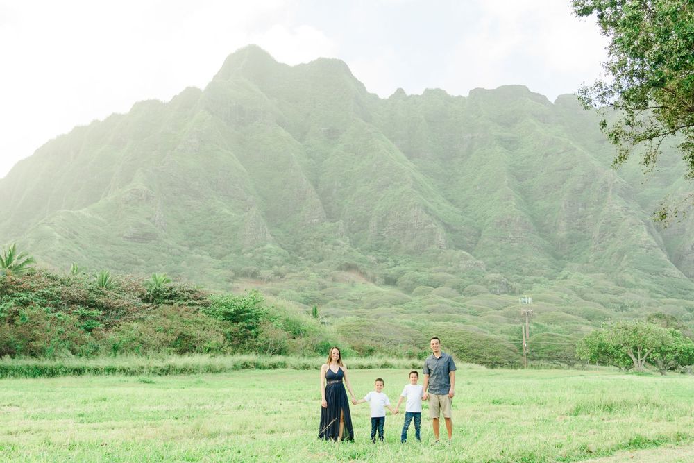 Group standing together in a grassy field with the dramatic Ko'olau Mountains of Hawaii in the background.Oahu Family Photographer