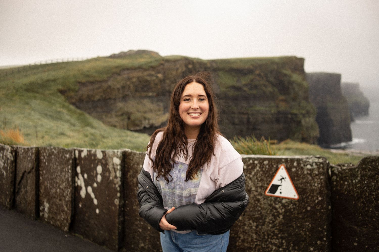 A woman stands at the scenic Cliffs of Moher in Ireland on a misty day.