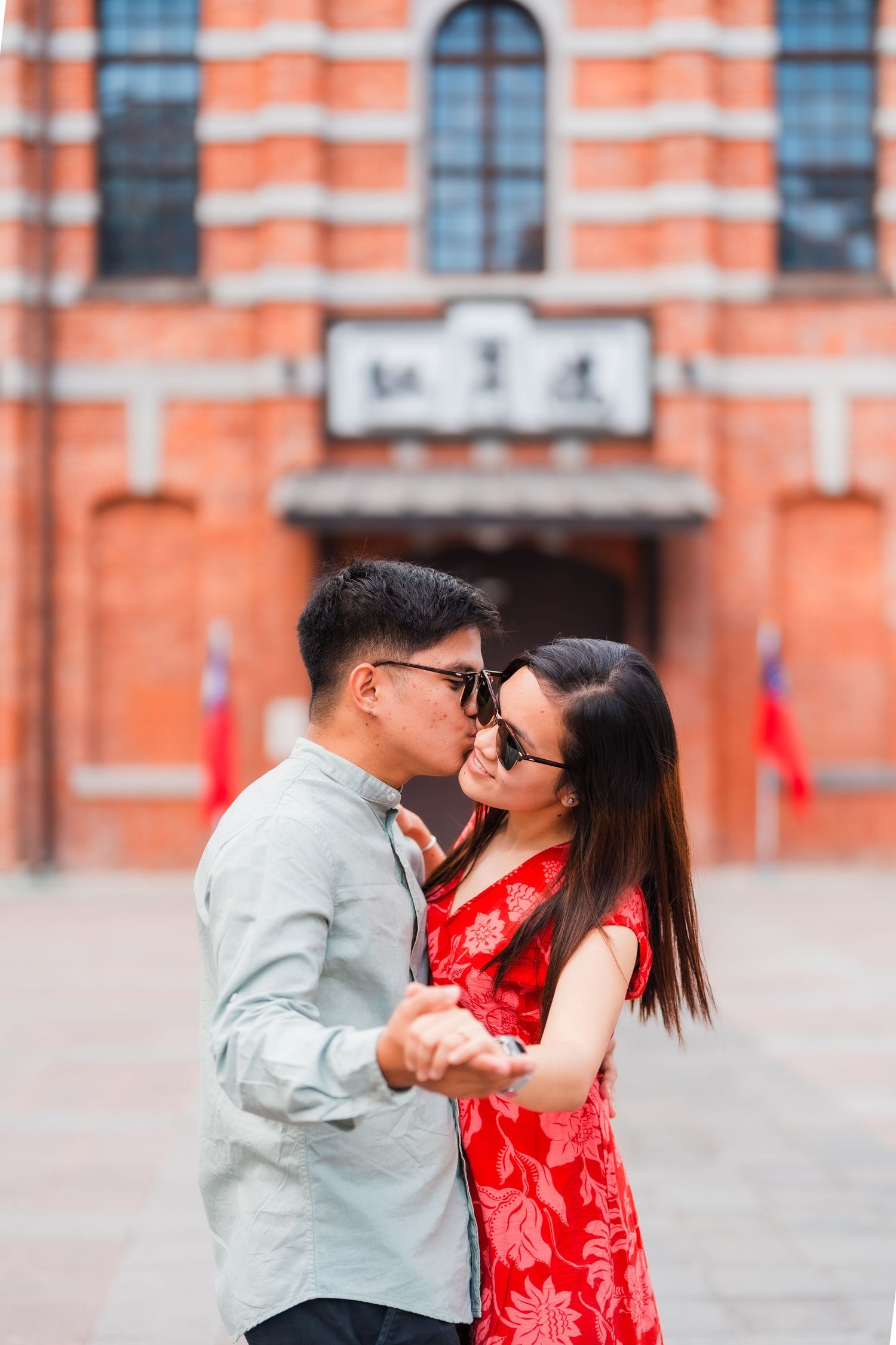 A couple embracing in front of a striped orange building with arched windows.