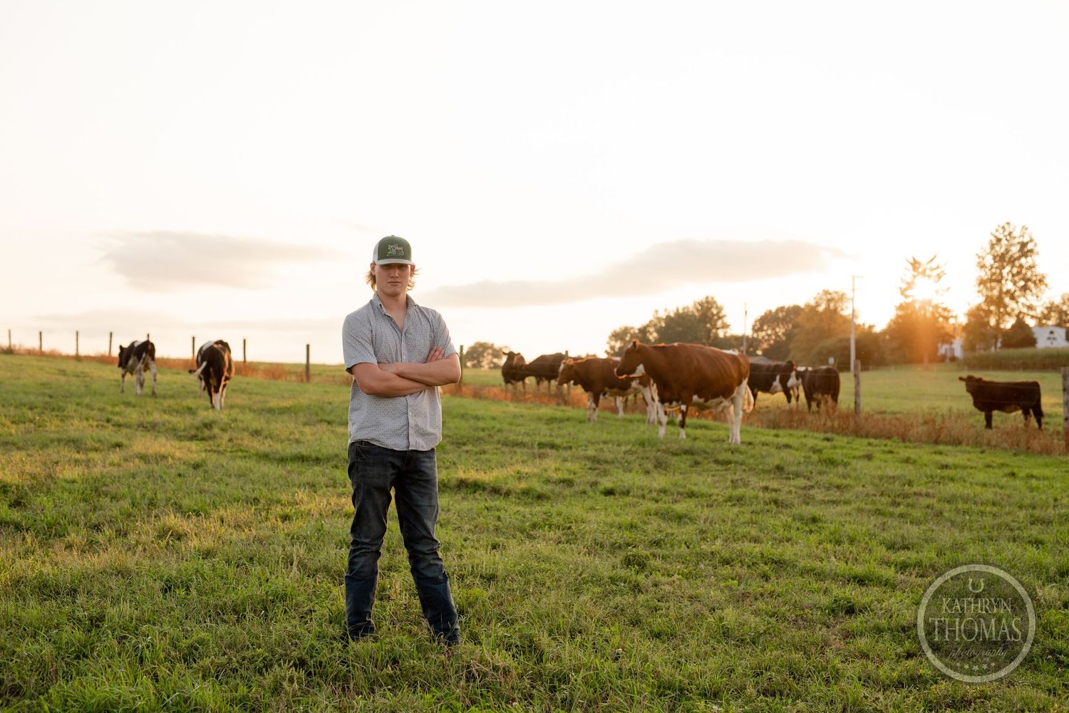 Rural scene of a farmer standing in pasture with grazing cattle during sunset.
