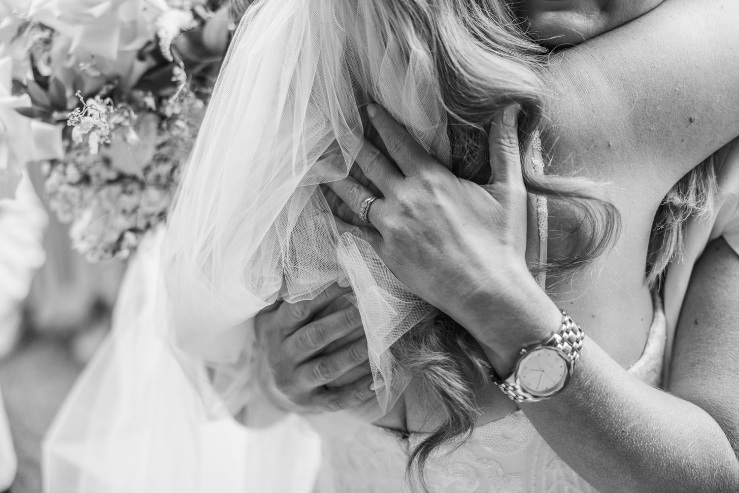 Close-up black and white shot of hands with rings and bracelet against wedding dress.