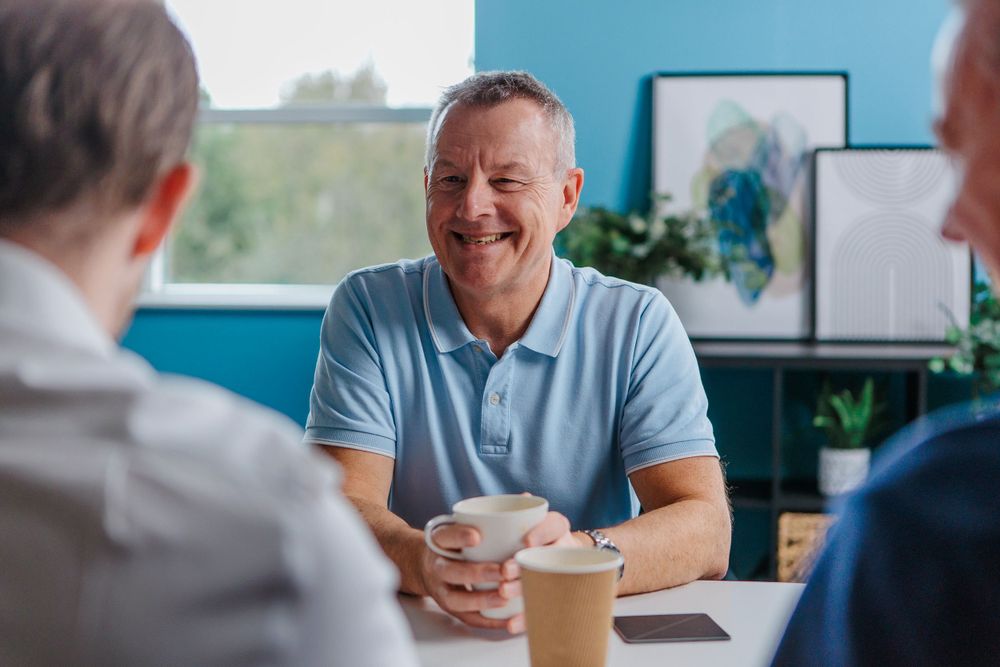 A person smiles during a casual business meeting over coffee in a bright office setting.