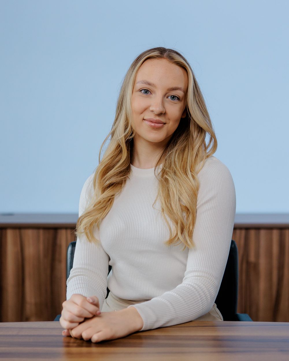 Professional portrait of person in white sweater seated at wooden table.