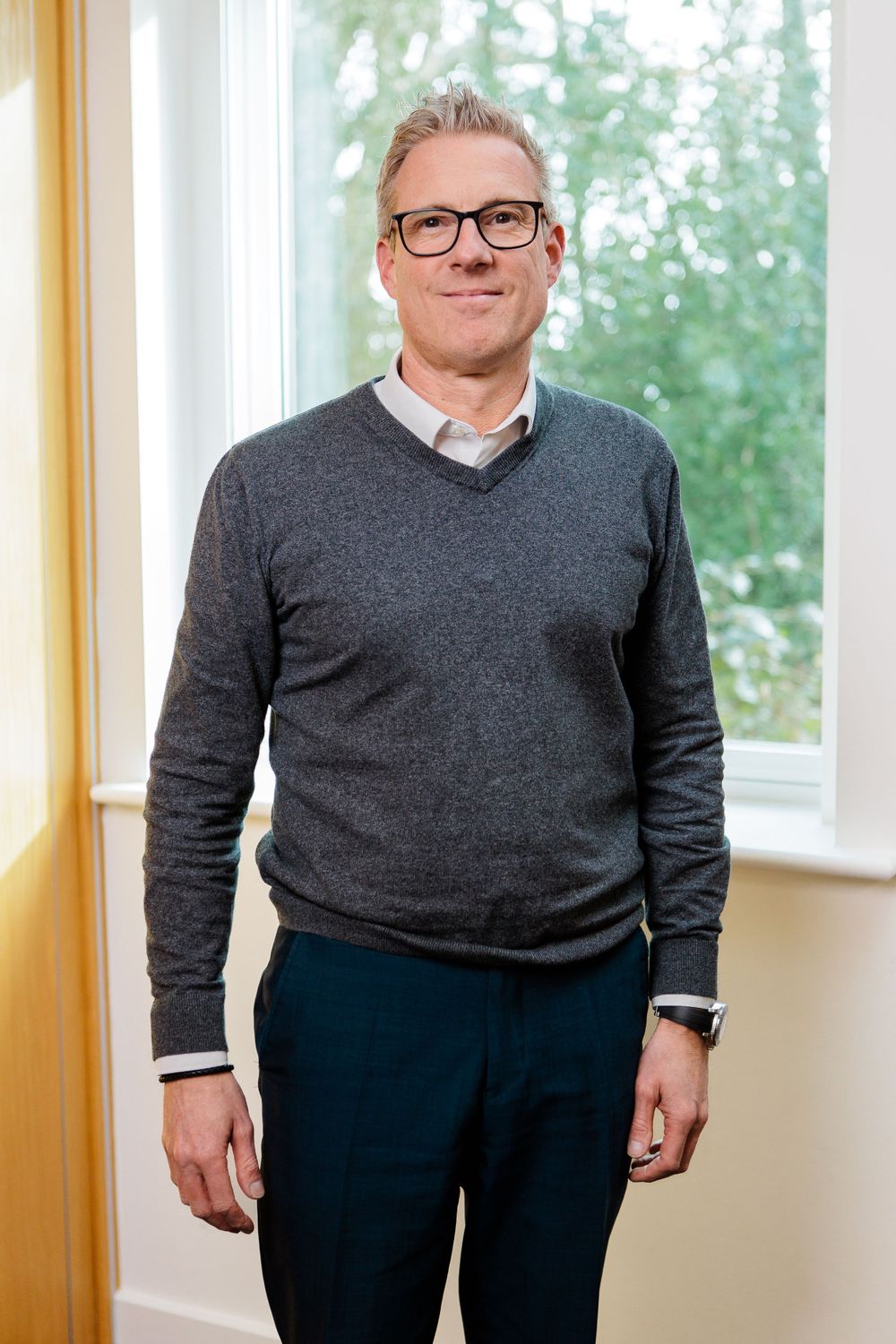 Professional portrait of person in grey sweater and glasses by window.